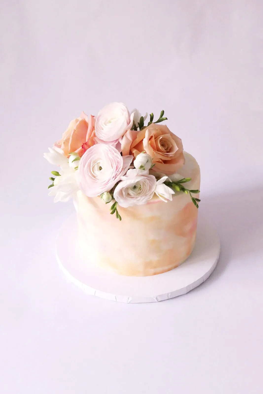 A soft blush cake topped with cream and peach flowers